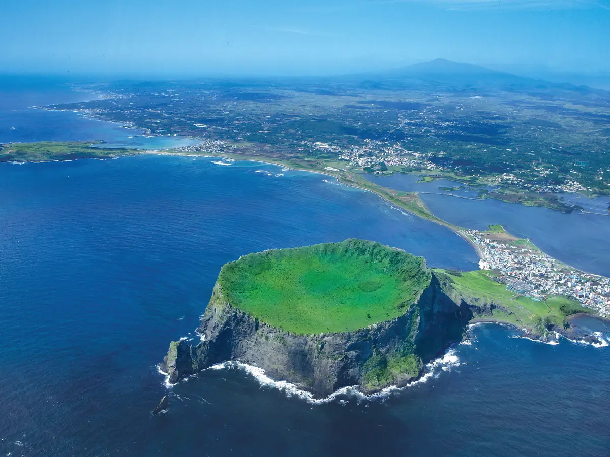 Aerial view of the green Seongsan Ilchulbong volcanic crater rising from the sea on Jeju Island