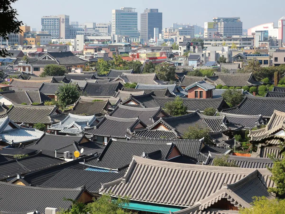 Rows of dark tiled hanok rooftops in Jeonju Hanok Village with the modern city behind